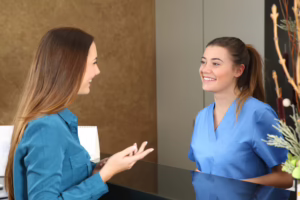 Nurse Speaking With Patient At Clinic Reception Desk