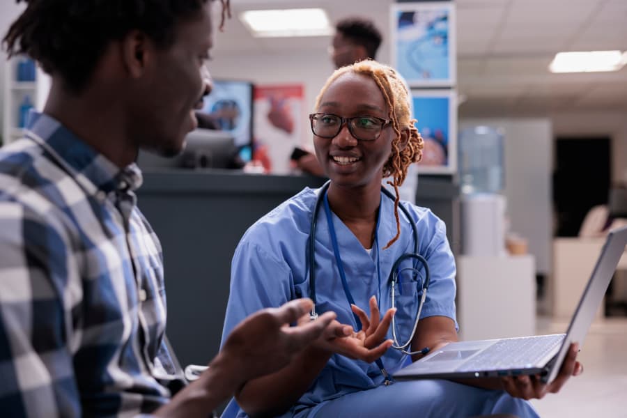 Nurse consulting patient at clinic sitting in waiting room lobby and using laptop