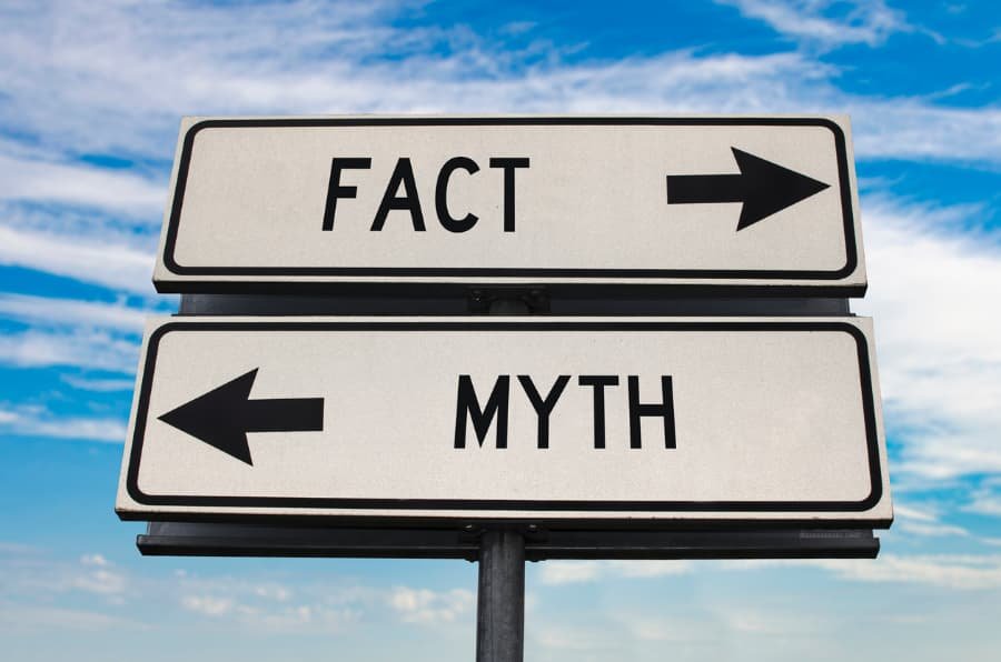 White street sign, pointing in one direction toward “fact” and another toward “myth”