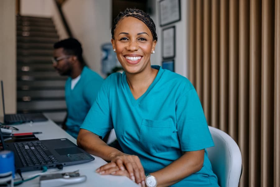 Female nurse sitting in front of computer and smiling with male nurse in background