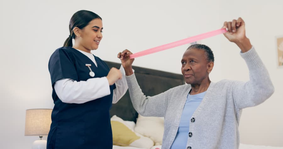 Medical assistant helps senior patient perform exercise with resistance band 