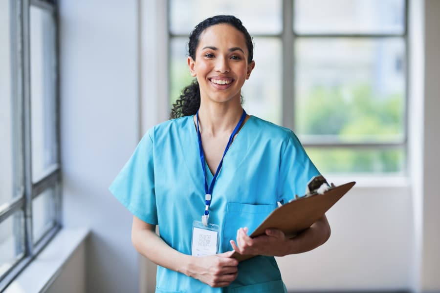 Smiling registered nurse in scrubs holding a clipboard