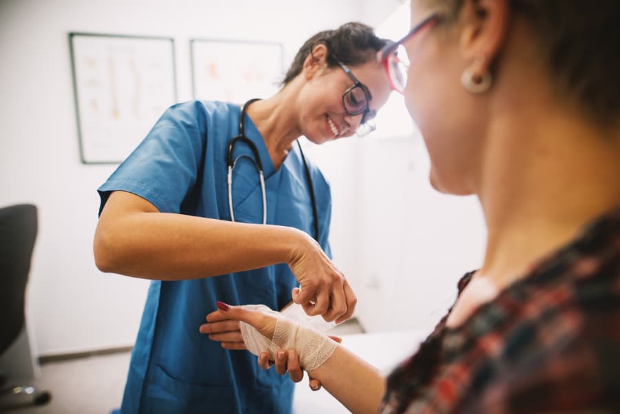 Medical assistant wrapping gauze on patient