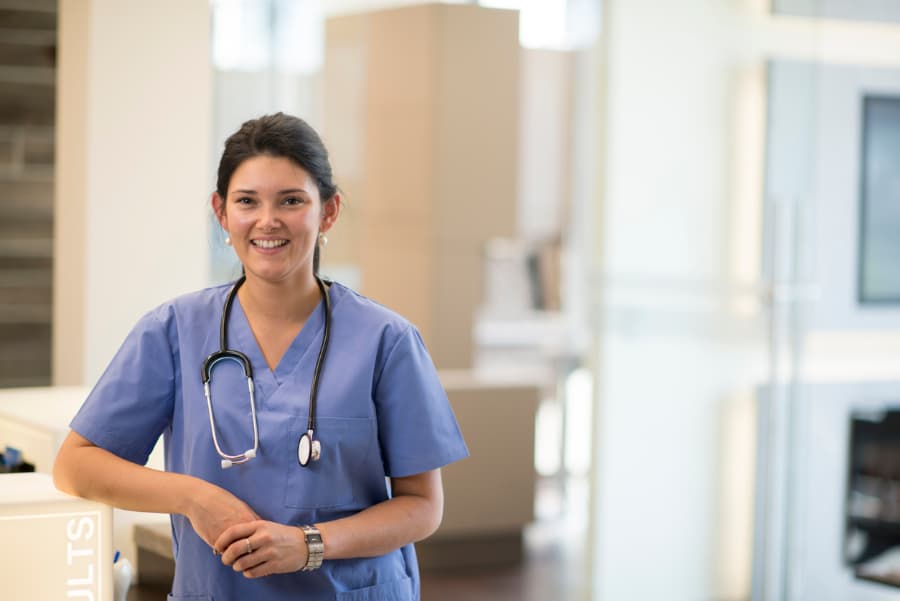 Medical assistant wearing blue scrubs and stethoscope around neck, smiling in clinic