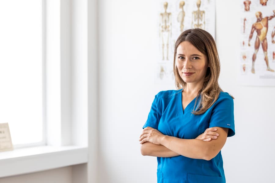Nurse wearing scrubs in hospital room with anatomy posters on wall
