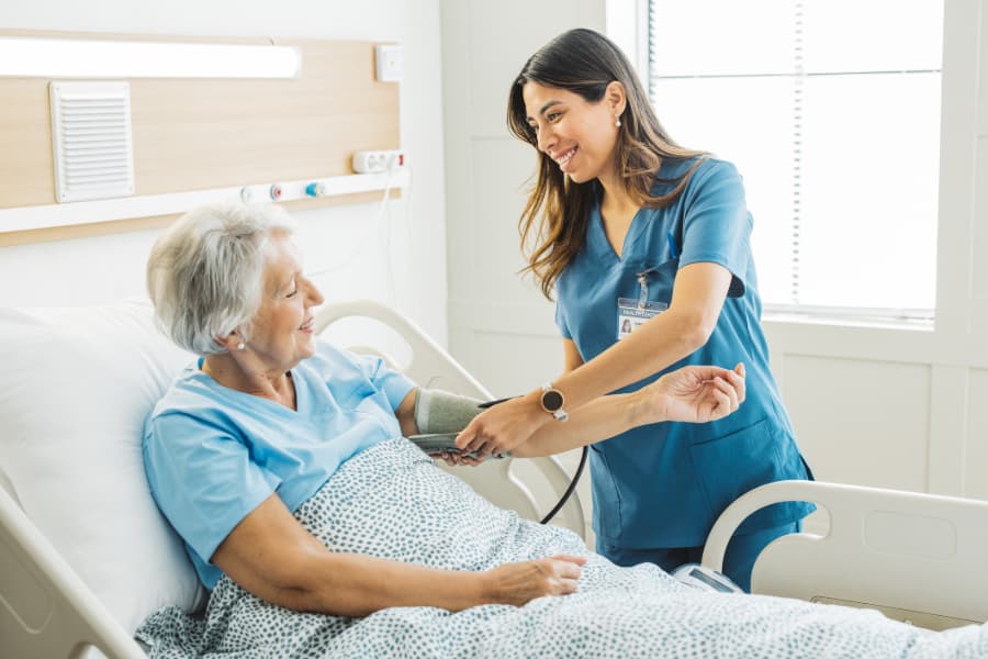Nurse talking to patient in hospital bed taking blood pressure reading