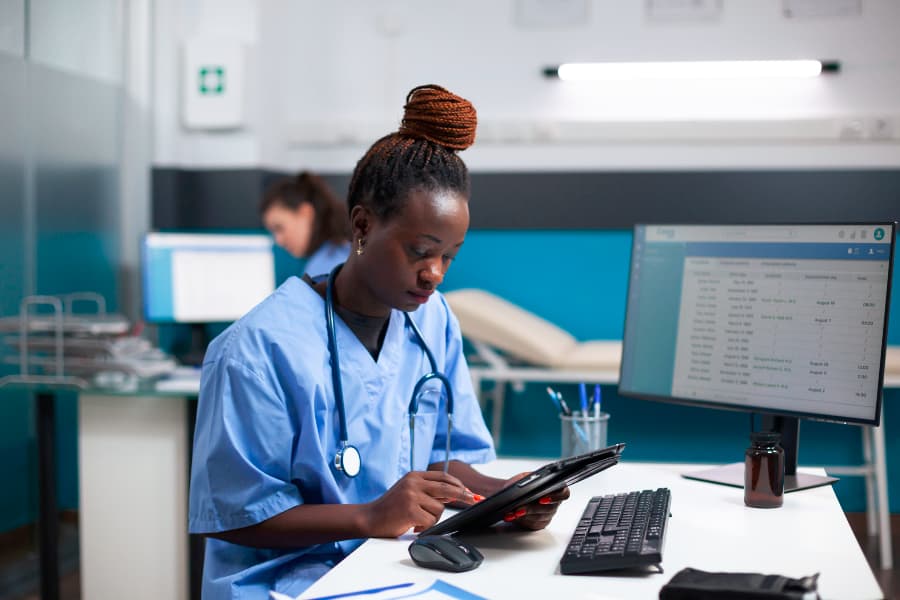 Nurse checking appointments list on digital tablet in busy medical office sitting at desk