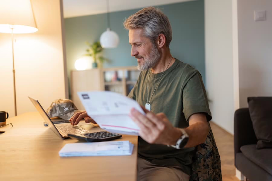 Military veteran sorting and paying bills from home on laptop in living room